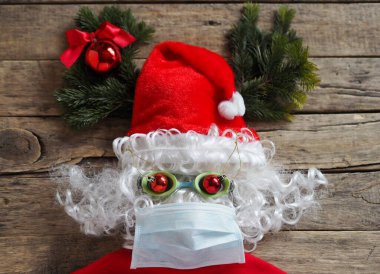 Noel Baba 'nın tıbbi maskeden yapılmış bir başlık ve tahta bir arka planda gözlük görüntüsü. Noel zamanı Covid 19 'u yakalamamak için koruyucu giysi kullanın. Kendine ve sevdiklerine iyi bak..