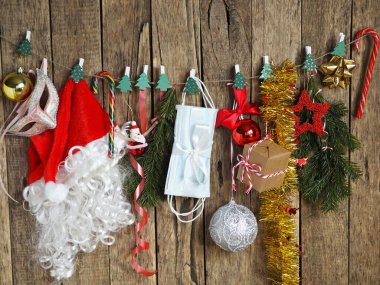 Noel 'de kendini koronavirüsten koru. Noel Baba şapkası ve Noel ağacı süslemeleri ahşap bir zemin üzerinde mandal ve tıbbi koruyucu maskelerle birlikte bir ipte asılı duruyor.