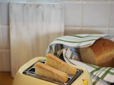 Mutfaktaki ekmek kızartma makinesinde ekmek kesme tahtası, ekmek ve mutfak peçetesinin arka planında. Sağlıklı moda kahvaltı yemekleri.