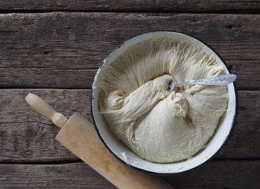 Ev yapımı yemek. Havai maya hamuru mavi bir kasede, ahşap bir arka planda merdaneyle..