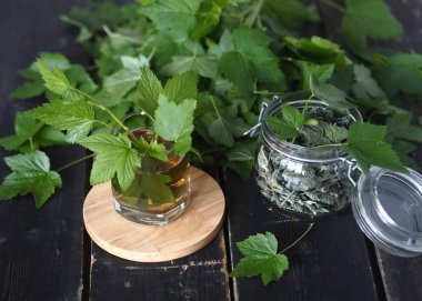 Kurutmak ve çay olarak kullanmak için taze frenk üzümü yaprakları hazırlıyoruz. Taze frenk üzümü yaprakları, bir kavanoz kuru yaprak ve koyu ahşap bir masada çay..