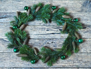 Ağacın dallarından, konilerden ve oyuncak toplardan oluşan Noel çelengi ahşap bir arka planda.