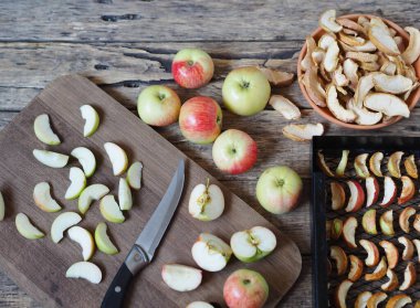 Kurutulmuş meyve toplama mevsimi. Elma cipsi, taze elma ve kurutucudaki kuru dilimler ahşap bir arka planda..