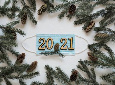 Beyaz arka planda yeşil ladin dallarıyla çevrili 2021 numaralı tıbbi yüz kalkanı. Yeni yılda veya Noel 'de yeni bir konsept. Salgın sırasında tatiller..