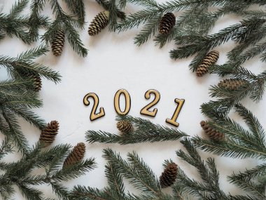 Yılbaşı arkaplanı, tebrik mesajları ve 2021 numaralar. Noel ağacı dalları beyaz arka planda serilmiştir..