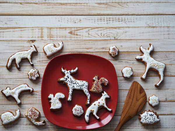 Homemade Christmas cookies in the shape of animals are laid out on a red plate on a wooden background. New year's table decoration.