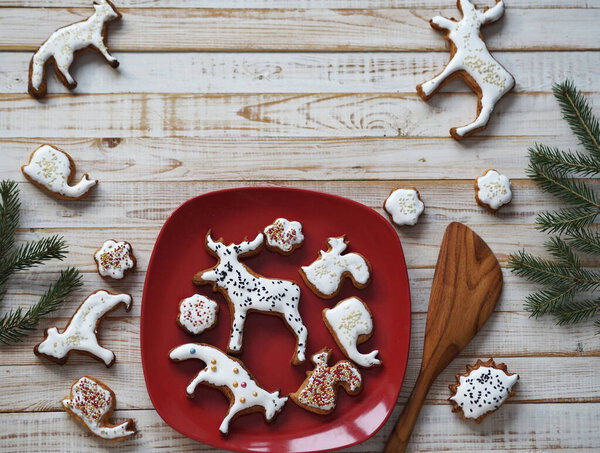Homemade Christmas cookies in the shape of animals are laid out on a red plate on a wooden background with fir branches. New year's table decoration.