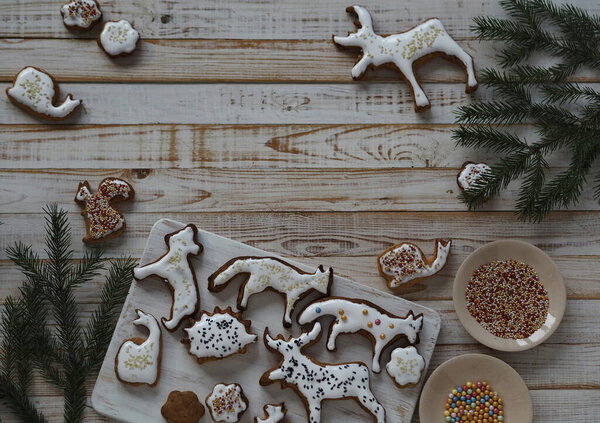 Homemade Christmas cookies in the shape of animals are laid out on a wooden background with fir branches. Christmas edible decor.