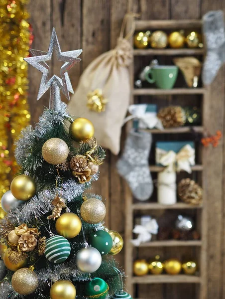 Ozdobiona choinka w żółto-zielonym stylu na rozmytym tle drewnianej starej półki z dekoracjami świątecznymi, kulkami, świecidełkiem, filiżanką kawy z domowymi ciasteczkami, rożkami jodłowymi. — Zdjęcie stockowe