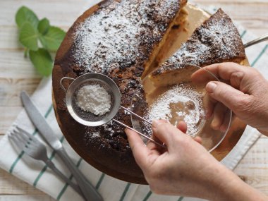 Yaşlı bir kadının elleri çaya pudra şekerli çikolata parçacıkları serpiyor. Ev yemeği pişirme süreci. Doğal sağlıklı yiyecekler.