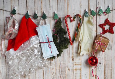 Tıbbi maskeli, eldivenli, gözlüklü ve el dezenfektanlı Noel Baba şapkası kırmızı örgü üzerine serili. Noel döneminde Covid 19 'u yakalamamak için koruyucu ekipman kullanın.