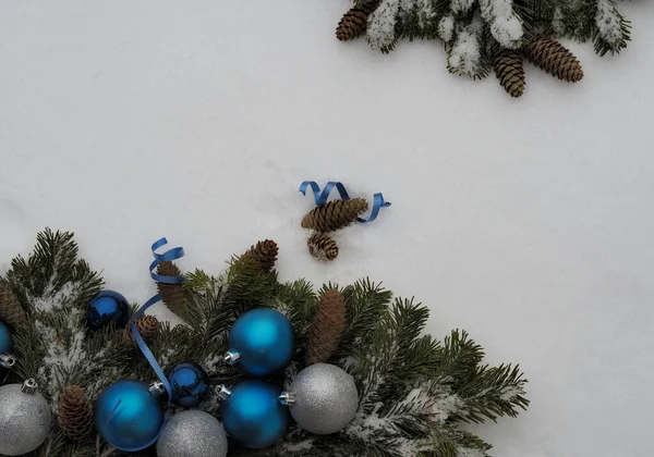 Χριστουγεννιάτικο φόντο για ευχετήριες επιστολές. Σπρους κλαδιά με κώνους και την Πρωτοχρονιά είναι διακοσμητικές μπάλες απλώνονται στο χιόνι. — Φωτογραφία Αρχείου