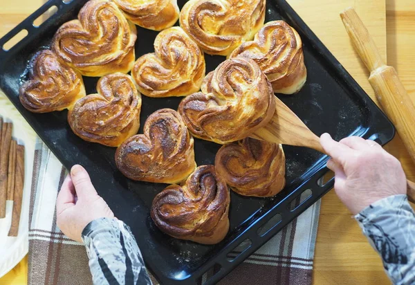 The process of baking homemade buns. A woman removes ready-made buns from a baking sheet from the kitchen oven. Home cooking. A woman is hobby.