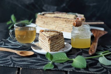 Koyu arkaplan üzerine katmanlı ballı kek. Nane dalları, yeşil çay ve koyu arkaplanda bal. Gıda arkaplanı.