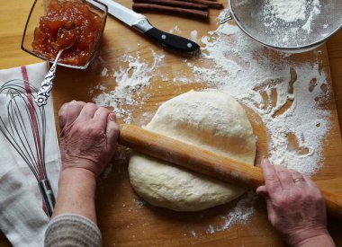 Yaşlı bir kadının elleri ahşap mutfak tahtasına hamur döküyor. Favori ve kullanışlı hobi. Ev yemeği..