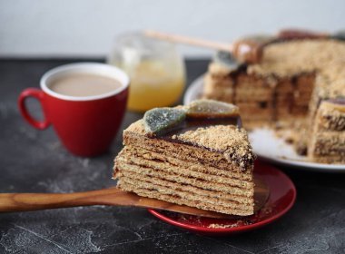 Kırmızı tabakta dilimlenmiş bir parça ballı kek ve koyu arkaplanda bir fincan kahve ve bal. Kırsal tarzda yiyecek arkaplanı.