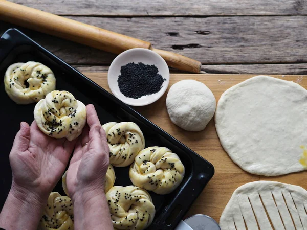 An elderly woman\'s hands form dough buns and place them on a baking sheet from the kitchen oven. Food background on a wooden ancient table.