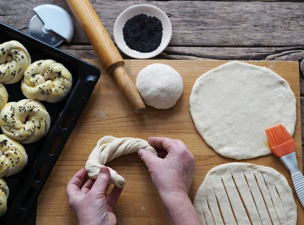 An elderly woman\'s hands form dough buns and place them on a baking sheet from the kitchen oven. Food background.