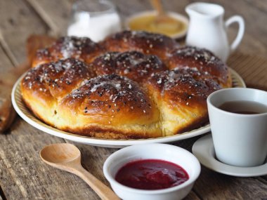 Ev yapımı kek. Reçel dolgulu çörekler, susam ve krema serpiştirilmiş şeker, eski ahşap bir arka planda, malzemeler ve bir fincan çay.