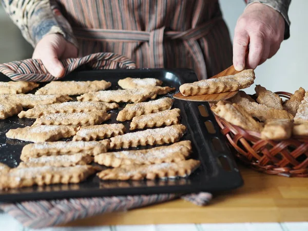 Homemade cookie concept. The hands of an elderly woman remove the prepared freshly baked cookies from the baking sheet onto a plate. Blurred foreground.