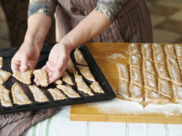 Homemade cookie concept.An elderly woman is hands place sliced raw biscuits on a baking sheet in the oven.