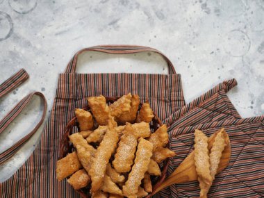 Ev yapımı kurabiye fikri. Mutfak önlüğü ve fırın eldiveni önünde hazır pişmiş taze kurabiyelerle doğal hasır kaplama. Bulanık arkaplan.