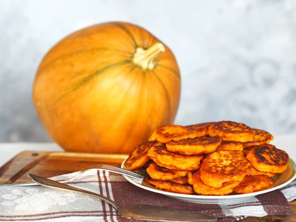Diet healthy food idea. Fried pumpkin pancakes in a plate on the background of a large orange pumpkin.