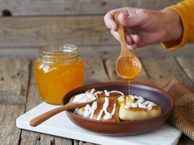 Yaşlı bir kadının eli kızarmış çöreğin üzerine bal döküyor. Sağlıklı ev yapımı yiyecekler..