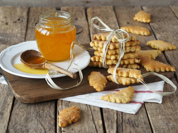 Wooden spoon with a jar of natural rustic honey and a stack of homemade cookies on a wooden background. The concept of the health benefits of honey.