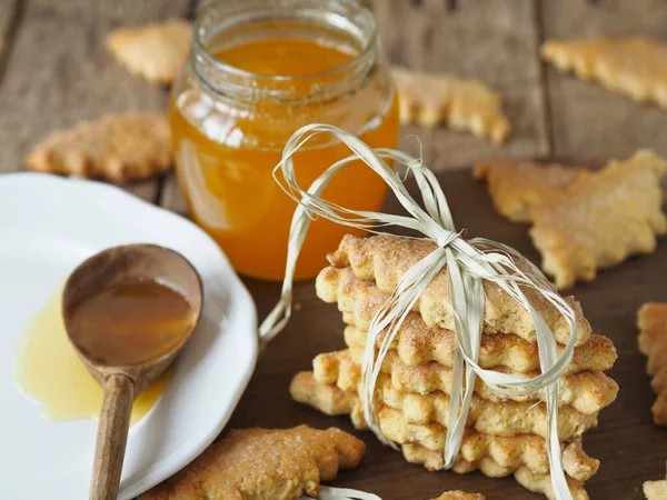 Wooden spoon with a jar of natural rustic honey and a stack of homemade cookies on a wooden background. The concept of the health benefits of honey.