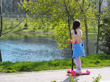 Spring warm day off. Children walk and ride scooters in a city park in nature.