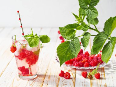 Raspberry tonic with ice and mint on a light wooden background with raspberry leaves.
