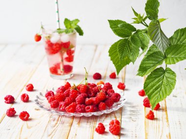 Summer background with a drink. A glass of tonic with raspberries and ice with a background of raspberry leaves. Quench your thirst in hot summer.