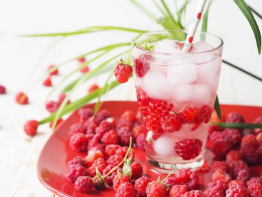 Summer background with a drink. A glass of tonic with raspberries and ice on a red plate. Quench your thirst in hot summer.