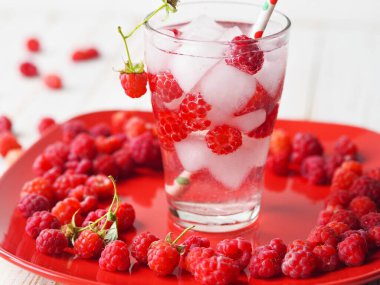 Summer background with a drink. A glass of tonic with raspberries and ice on a red plate. Quench your thirst in hot summer.