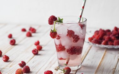 A tonic drink with ice and raspberries. onik. A glass of summer drink on a light wooden background.