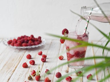 A tonic drink with ice and raspberries. onik. A glass of summer drink on a light wooden background.