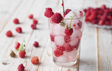 A tonic drink with ice and raspberries. onik. A glass of summer drink on a light wooden background.