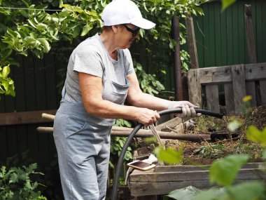 Özel bir sebze bahçesinin köşesindeki gübre yığınında doğal geri dönüştürülmüş ev yapımı gübre. Bir kadın organik gübrelerin en hızlı hazırlanması için bir yığın suyu suluyor..