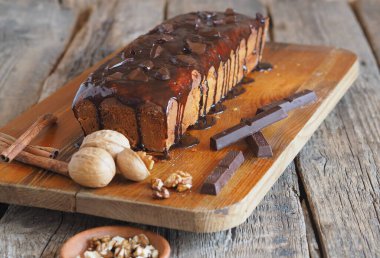 Çikolata şenlikli balkabağı uzun dikdörtgen kek, çikolatayla kaplı, mutfak tahtasının üzerinde yemek için malzemelerle birlikte hazır. Ahşap antik bir arkaplan.