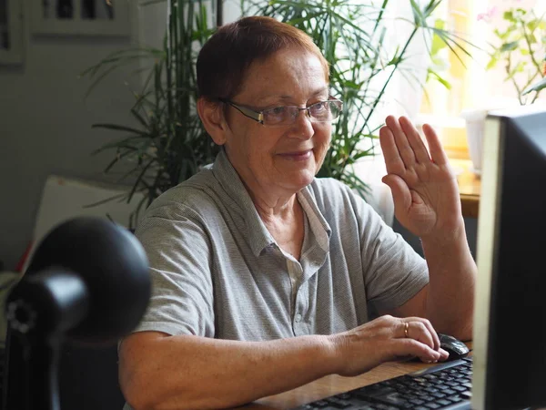 An elderly woman, working on a computer, calls on the phone. Online communication with loved ones, quarantined work or an elderly woman\'s hobby.