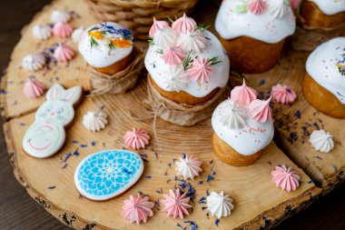 Hristiyan Paskalyası 2021. Kurabiye ve çiçeklerle süslenmiş paskalya pastaları, doğal ahşap arka planda bir sepete boyanmış yumurtalar..