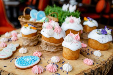 Hristiyan Paskalyası 2021. Kurabiye ve çiçeklerle süslenmiş paskalya pastaları, doğal ahşap arka planda bir sepete boyanmış yumurtalar..