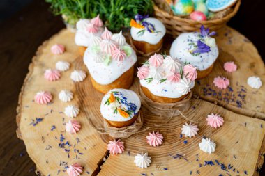 Paskalya dekoru 2021. Beyaz kremalı, kremalı ve çiçekli kekler, kremalı zencefilli kekler ve doğal ahşap arka planda sepetin içinde renkli yumurtalar. Paskalya kartı.