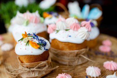 Paskalya dekoru 2021. Beyaz kremalı, kremalı ve çiçekli kekler, kremalı zencefilli kekler ve doğal ahşap arka planda sepetin içinde renkli yumurtalar. Paskalya kartı.