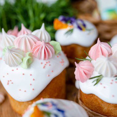 Paskalya dekoru 2021. Beyaz kremalı kekler, pembe bezeli, otlar ve çiçek yapraklarıyla süslenmiş arka planda doğal ahşap arka plan ve yeşillik. Paskalya kartı.