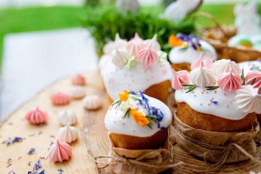 Ortodoks Paskalya 2021. Pasta dekorasyonu. Beyaz kremalı kekler, pembe ve beyaz kremayla süslenmiş, çiçekler ve doğal ahşap arka planda bitkiler. Paskalya kartı.