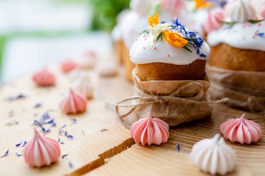 Ortodoks Paskalya 2021. Pasta dekorasyonu. Beyaz kremalı kekler, pembe ve beyaz kremayla süslenmiş, çiçekler ve doğal ahşap arka planda bitkiler. Paskalya kartı.