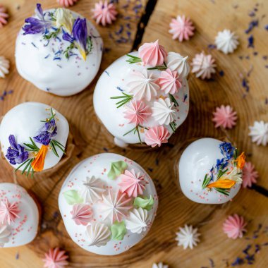 Ortodoks Paskalya 2021. Pasta dekorasyonu. Beyaz kremalı kekler, pembe ve beyaz kremayla süslenmiş, çiçekler ve doğal ahşap arka planda bitkiler. Paskalya kartı.