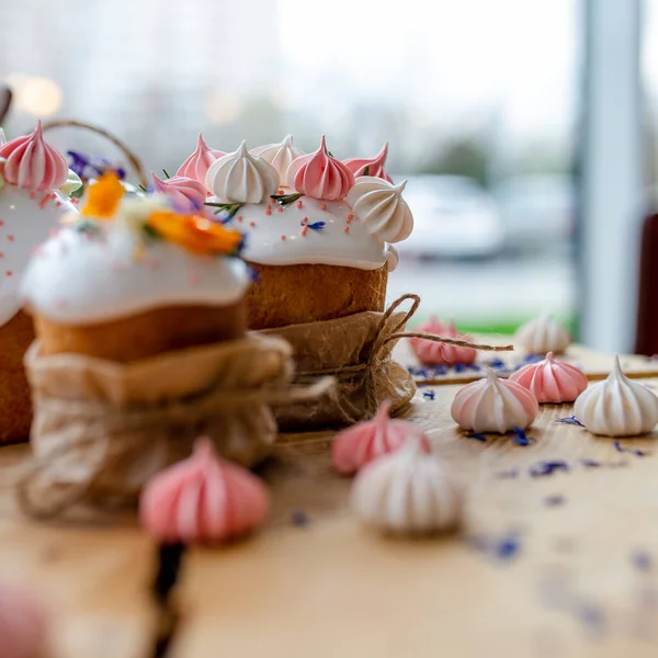 Ortodoks Paskalya 2021. Pasta dekorasyonu. Beyaz kremalı kekler, pembe ve beyaz kremayla süslenmiş, çiçekler ve doğal ahşap arka planda bitkiler. Paskalya kartı.